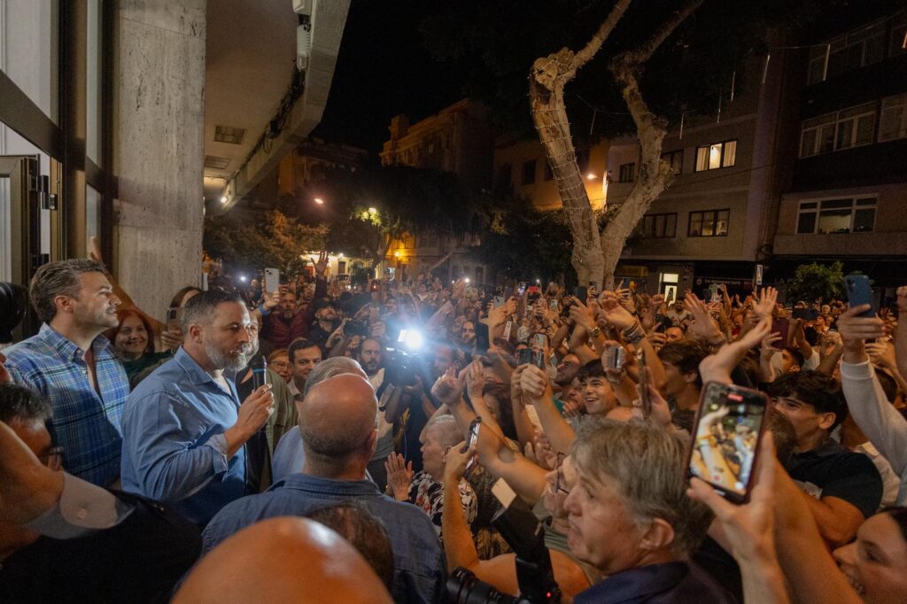 El presidente de VOX, Santiago Abascal, protagonizó este domingo una de las imágenes políticas más potentes del fin de semana en Las Palmas de Gran Canaria, donde más de 3.000 personas acudieron a escucharle. El Círculo Mercantil, con un aforo limitado a 400 asistentes, se llenó en apenas unos minutos, obligando al líder de VOX a salir a la calle e improvisar un mitin al aire libre ante una multitud que desbordó las calles aledañas. “Los canarios son patriotas, el cambio está llegando”, proclamó Abascal entre vítores y banderas españolas. Desde un altavoz improvisado, el líder de VOX agradeció el “cariño y la libertad” de los canarios y denunció que la Subdelegación del Gobierno tratara de “coartar” la asistencia a sus actos en Lanzarote y Arrecife. “Sentimos el apoyo de la gente porque no hemos traicionado a nadie, como sí ha hecho Pedro Sánchez”, afirmó. El líder de VOX acusó al Ejecutivo socialista de haberse “sostenido en la corrupción, el pacto con comunistas y terroristas, y la amnistía inconstitucional”. También denunció el uso político de la inmigración ilegal, asegurando que “traen a miles para regularizarlos y relegar a los españoles al último lugar”. En un tono más directo, señaló: “Mientras nuestros jóvenes se quedan sin casa ni futuro, nos dicen que debemos traer a los de fuera”. El momento más aplaudido llegó cuando Abascal prometió “llevar a Sánchez al banquillo”, entre gritos de apoyo y banderas ondeando. “Solo queda VOX”, sentenció, asegurando que puede caminar “con la cabeza alta” porque no se ha corrompido ni mentido. El acto fue inaugurado por Nicasio Galván, presidente provincial de VOX en Las Palmas, quien denunció el “sectarismo” del Parlamento canario y advirtió que “el tiempo del silencio se ha acabado”. También intervino Alberto Rodríguez Almeida, diputado nacional, que agradeció la presencia de Abascal y pidió “abrir los debates que la izquierda y el bipartidismo quieren cerrar”. El mitin de Abascal en Gran Canaria se ha convertido en una demostración de fuerza de VOX en el archipiélago y una señal clara de que el partido refuerza su implantación territorial con vistas a las próximas citas electorales.